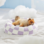 CozyPaw Donut Dog Bed – Modern Design, Soft & Warm, Washable Small dog lying on a checkered pet bed with a light blue wall in the background