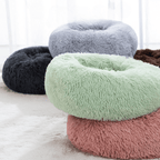 Four fluffy donut-shaped pet beds in different colors on a light surface.
