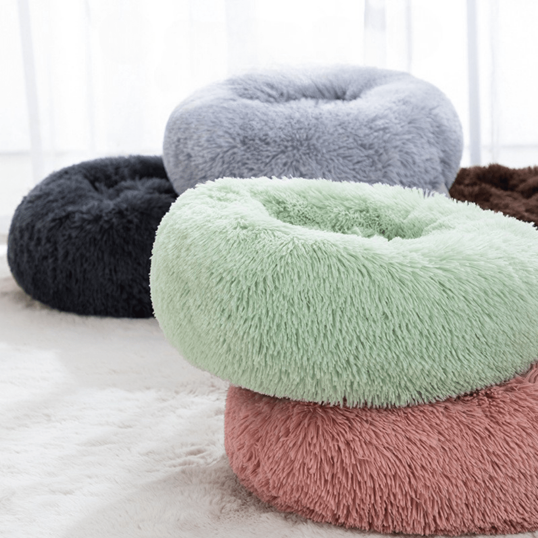 Four fluffy donut-shaped pet beds in different colors on a light surface.